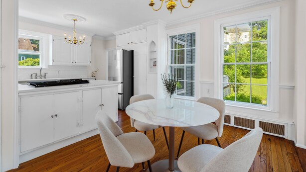 A modern kitchen with white cabinetry, a stainless steel refrigerator, and a dining table with chairs. - Historic Mystic Maritime House - 5 min Walk to Downtown Restaurants and Seaport (Mystic)