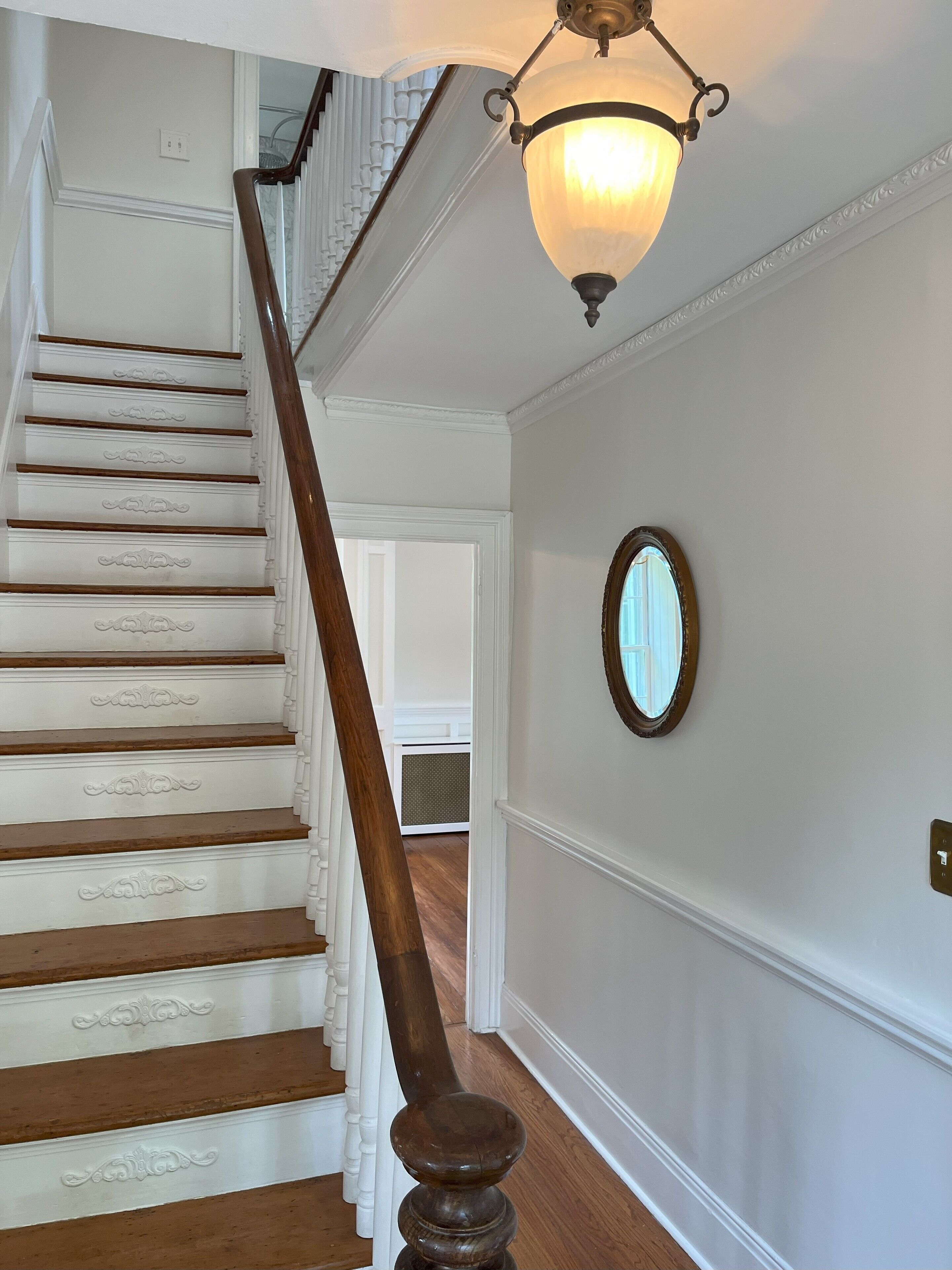 A staircase with ornate white railings and a wooden handrail, leading to a room with a large mirror on the wall.