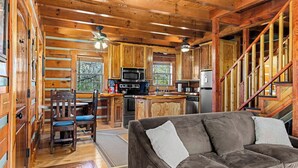 A cabin interior with wooden walls, a dining area, kitchen, and a sofa.