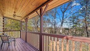 A wooden deck with a railing, a ceiling fan, and a view of trees.