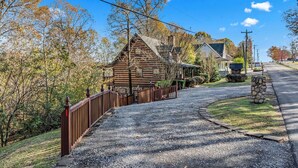A rural road leading to a wooden house with a gravel driveway and a stone wall.