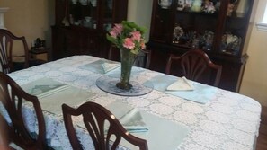 Une table à manger recouverte d’une nappe en dentelle, un vase rempli de fleurs et des chaises disposées autour.