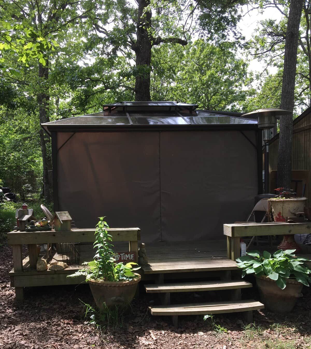 Un espacio al aire libre techado con un banco de madera y una mesa, rodeado de árboles.