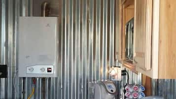 A compact kitchen with a built-in water heater, a coffee maker, and a shelf with various items.