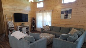 Una sala de estar acogedora con un sofá seccional gris, un televisor de pantalla plana, una escalera de madera y una planta decorativa.