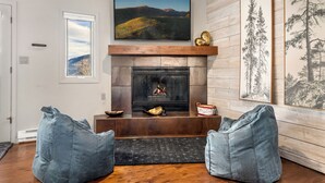 Una sala de estar con chimenea, dos sillones de tela y cuadros en la pared.