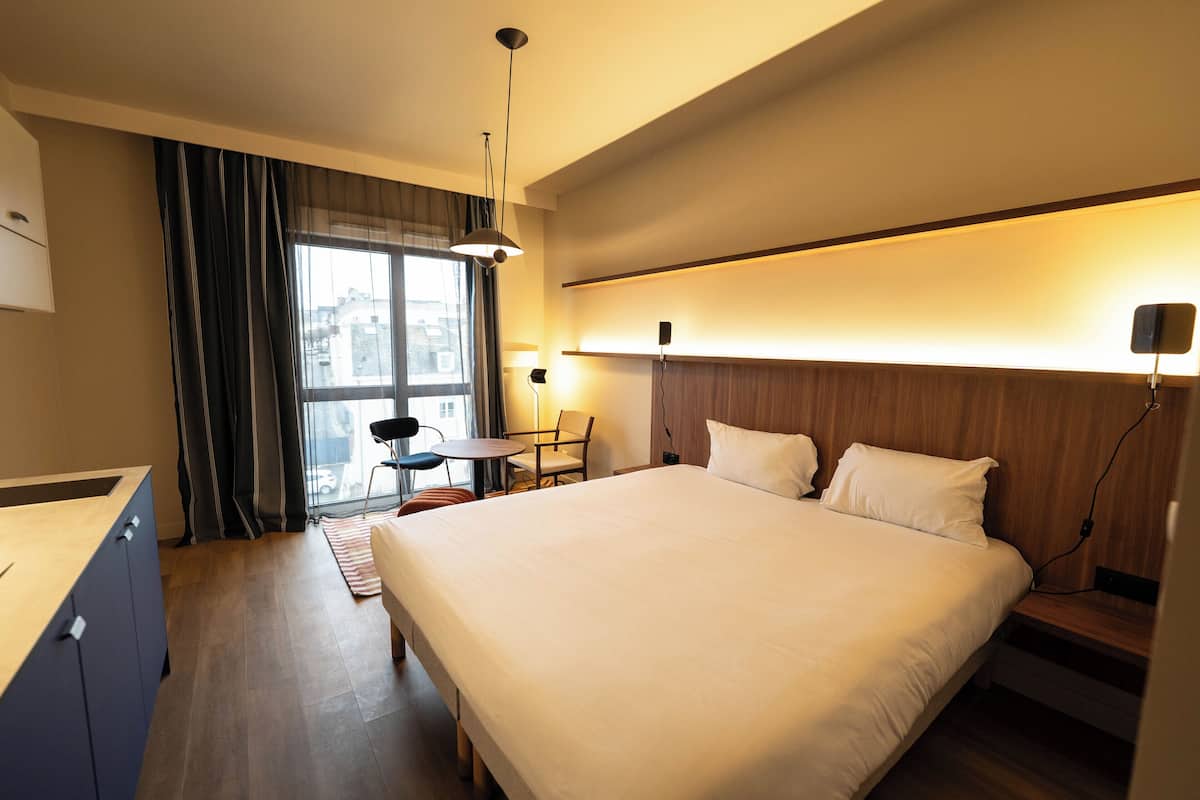 Une chambre d’hôtel moderne avec un grand lit, un bureau, une chaise et une fenêtre avec des rideaux.