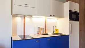 A modern kitchen with white cabinets, a blue countertop, a Bosch microwave, and a coffee machine. - Harvey Chartres — Résidence lifestyle 4★, Restaurant, Bien-Être, Sport & Déconnexion (Chartres)