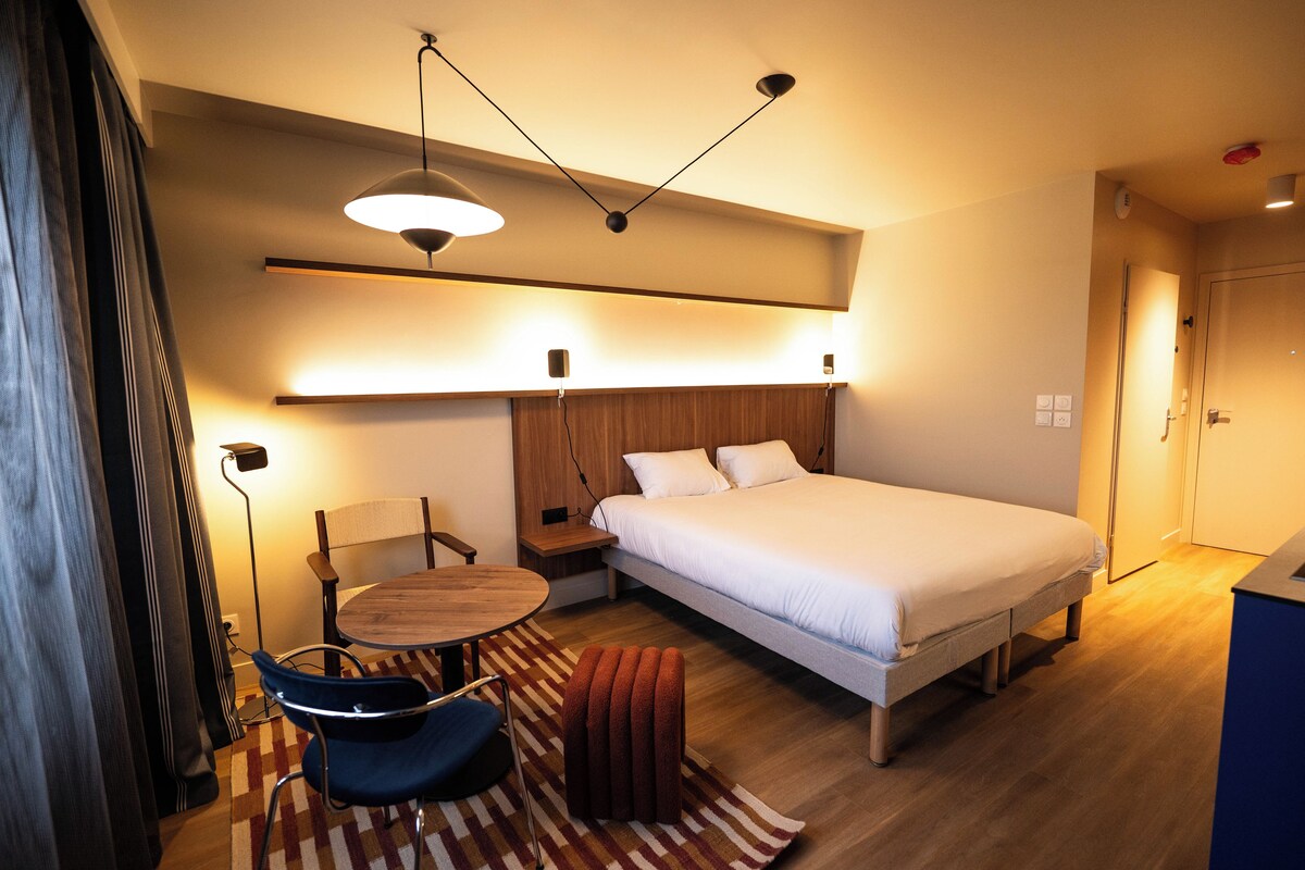 Une chambre d’hôtel comprenant un lit, une table de chevet, une chaise et une petite table ronde.
