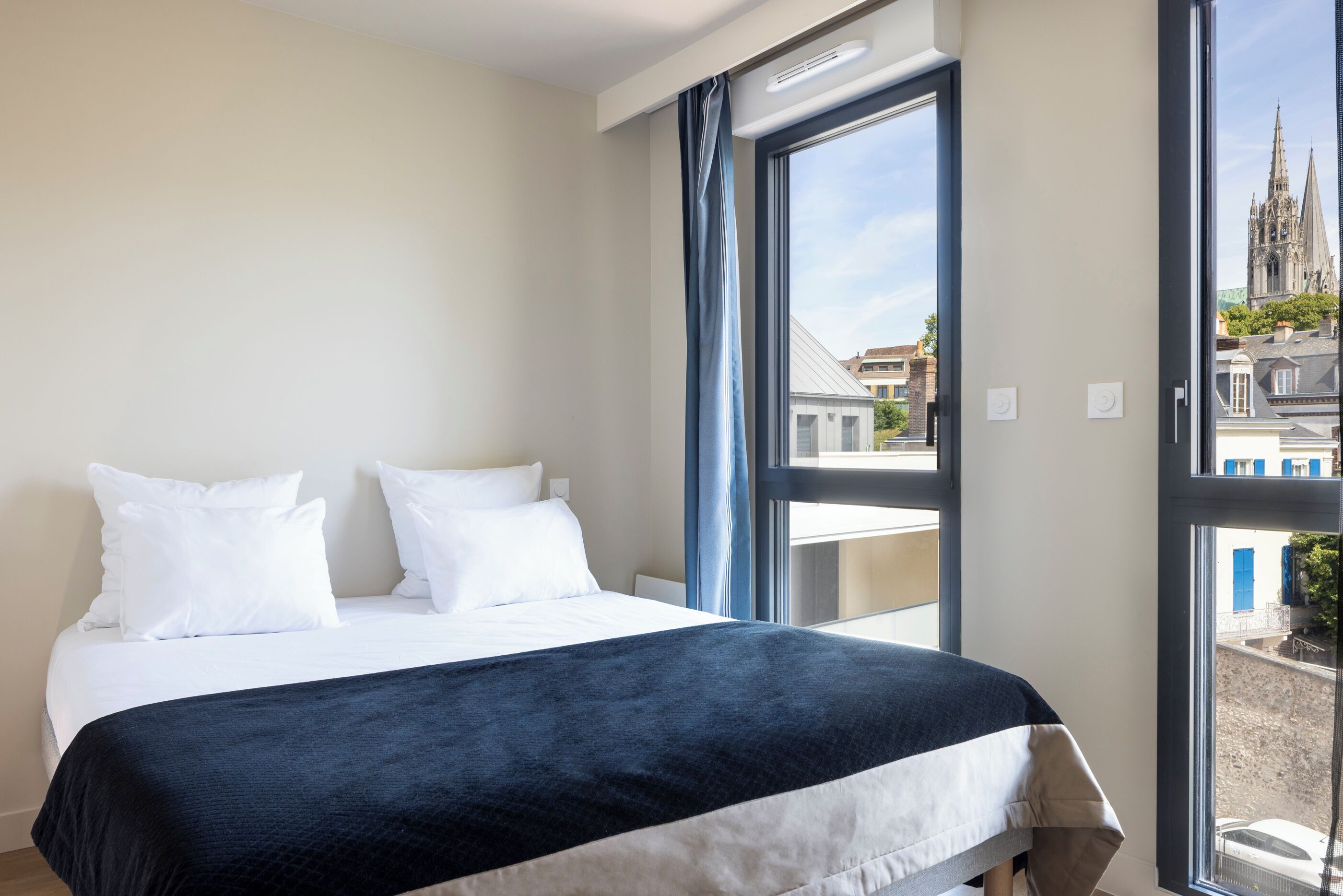 Habitación de hotel con una cama grande, vista de una catedral por la ventana y un balcón con barandilla.