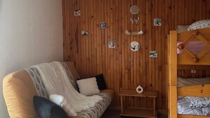 A cozy room with a wooden wall, a sofa, a small table, and a bunk bed. - Cosy Studio 4 people - Valmorel hamlet (Les Avanchers-Valmorel)