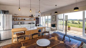 A spacious kitchen with a wooden dining table, built-in shelves, and a view of the countryside.