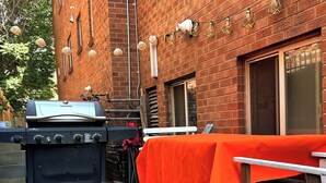 Un espace barbecue extérieur avec un gril et une table recouverte d’une nappe orange.