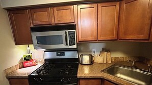 Une cuisine avec des meubles de rangement en bois, un évier en acier inoxydable, un four à micro-ondes, une cuisinière et un grille-pain.