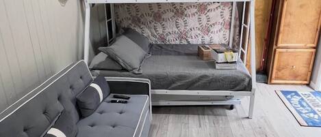 A bunk bed with a patterned headboard, a sofa with cushions, and a small table with a box.