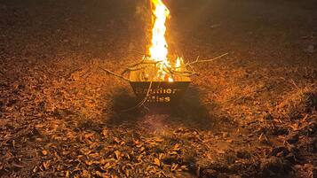 A campfire in a metal fire pit surrounded by dry leaves on the ground.