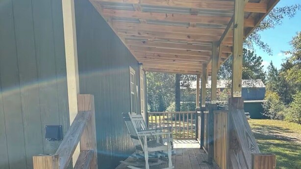 Une terrasse en bois avec un banc et une table, qui donne sur un espace de véranda abritée.