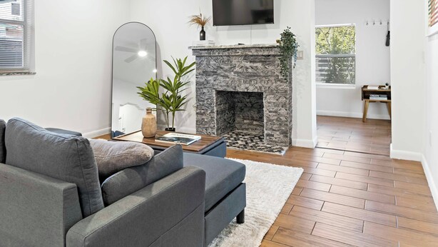 A modern living room with a grey sofa, a stone fireplace, a mounted TV, and a large mirror. - Stylish 2BR/2BA Home near Wynwood (Miami)