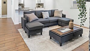 A modern living room with a grey sectional sofa, a wooden coffee table, and a white shag rug. - Stylish 2BR/2BA Home near Wynwood (Miami)