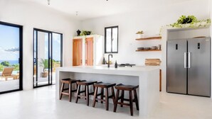 Una cucina moderna con isola centrale, sgabelli da bar, un frigorifero e vista sull'esterno.