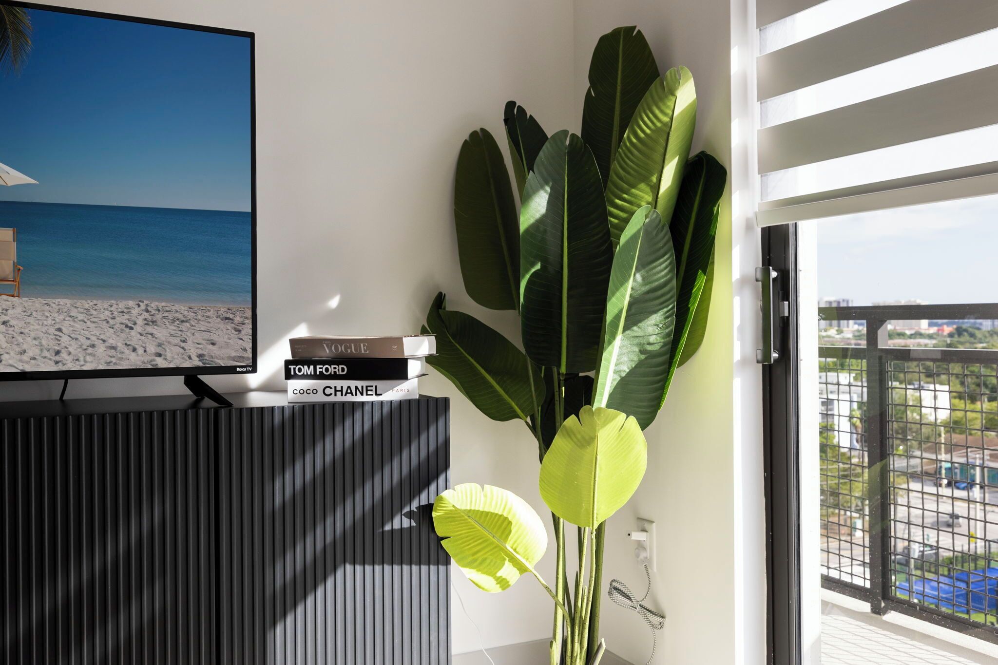 Un salon moderne doté d’un grand téléviseur à écran plat diffusant une scène de plage, d’une bibliothèque remplie de livres et d’une grande plante.
