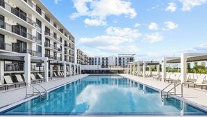 A modern hotel with a large rectangular pool, multiple balconies, and sun loungers.
