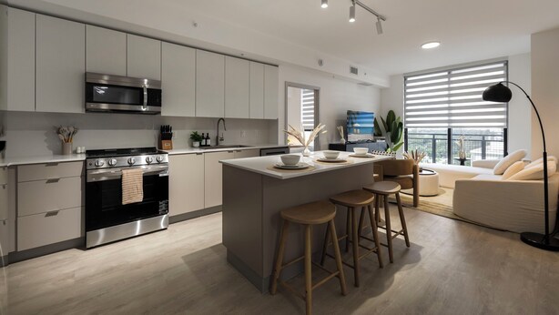A modern kitchen with a central island, bar stools, and a large window with blinds.