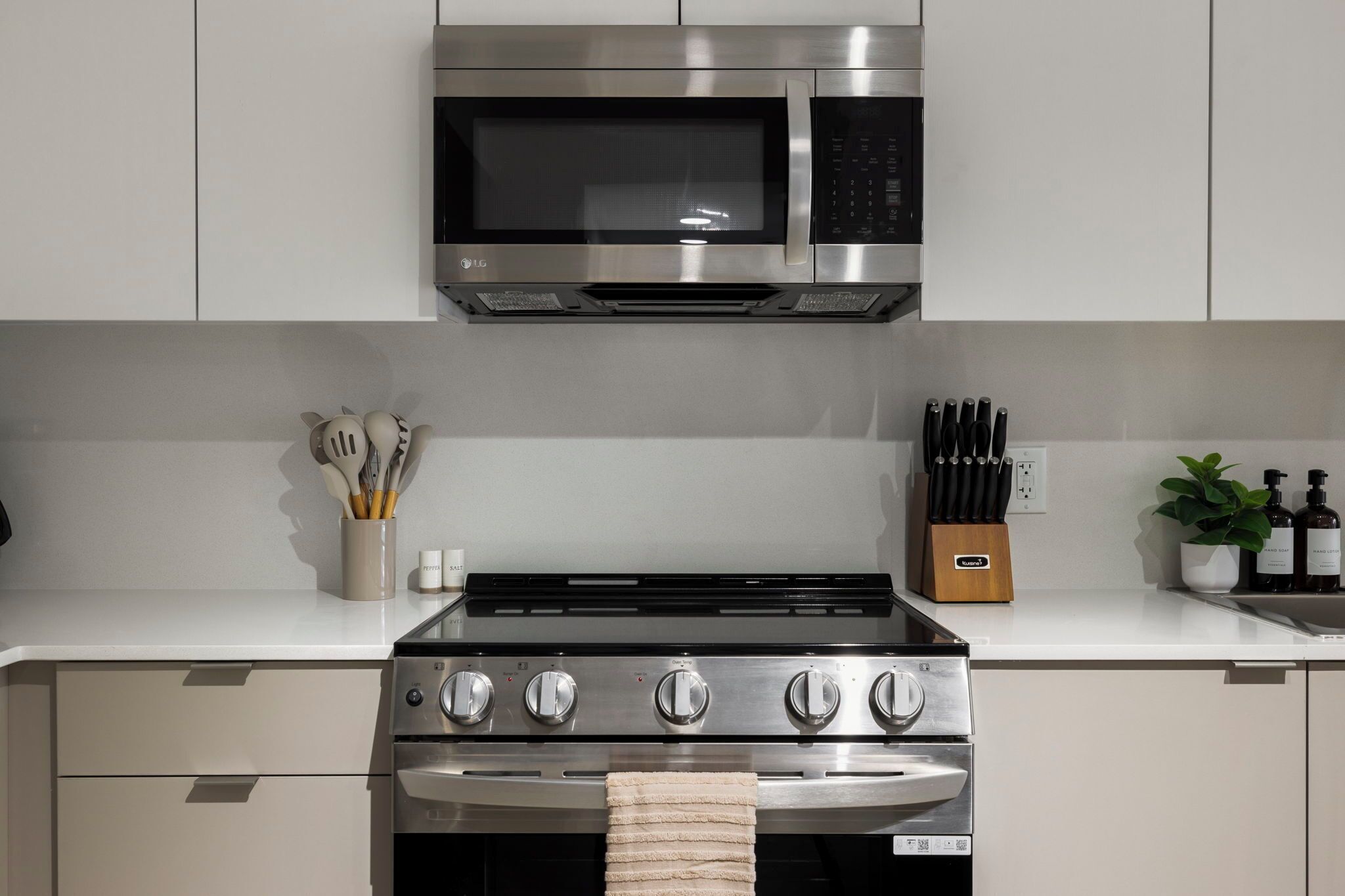 A modern kitchen with a stainless steel microwave, a gas stove, and a knife block.