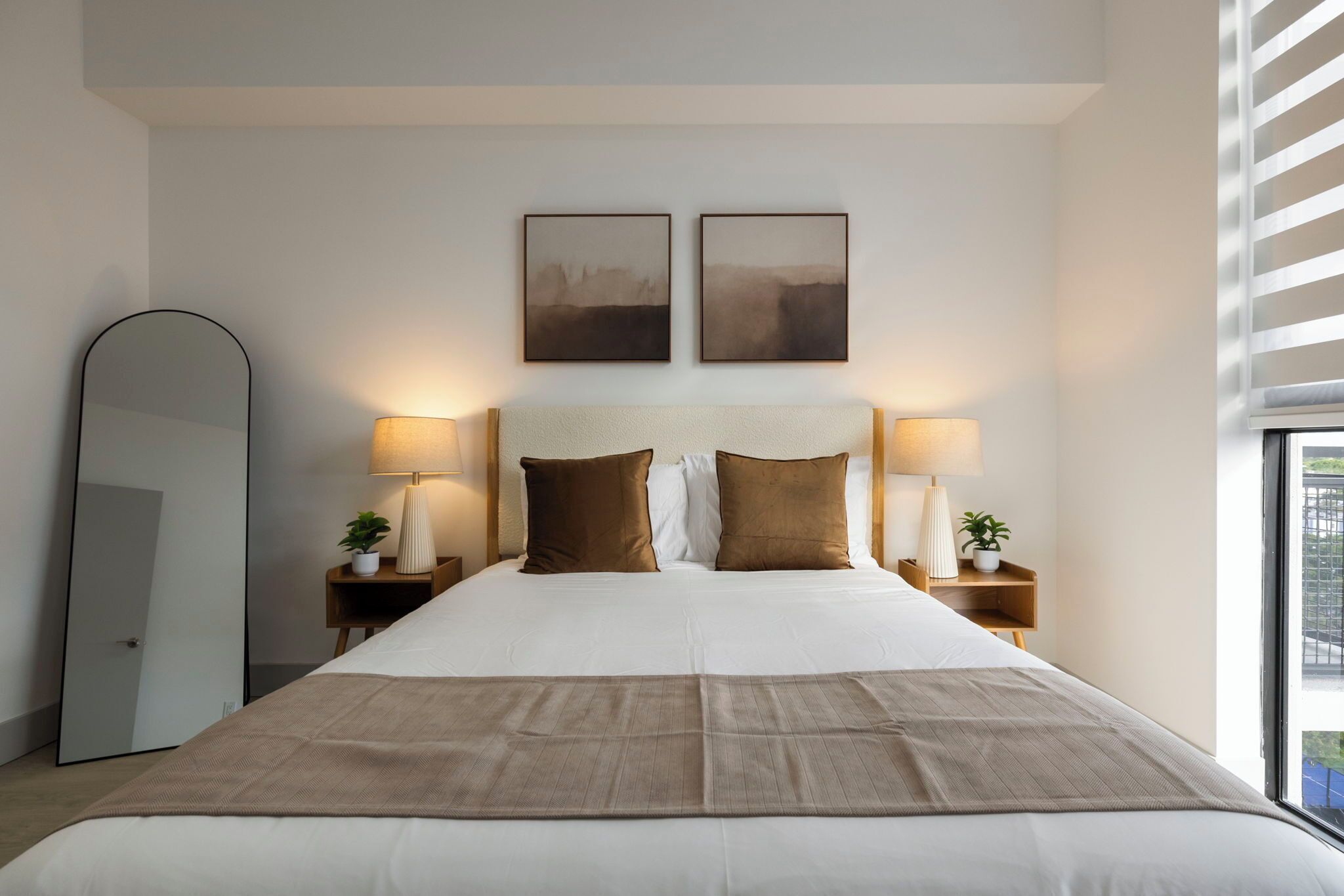 Een keurig opgemaakt bed met een grote spiegel en twee wandlampen.