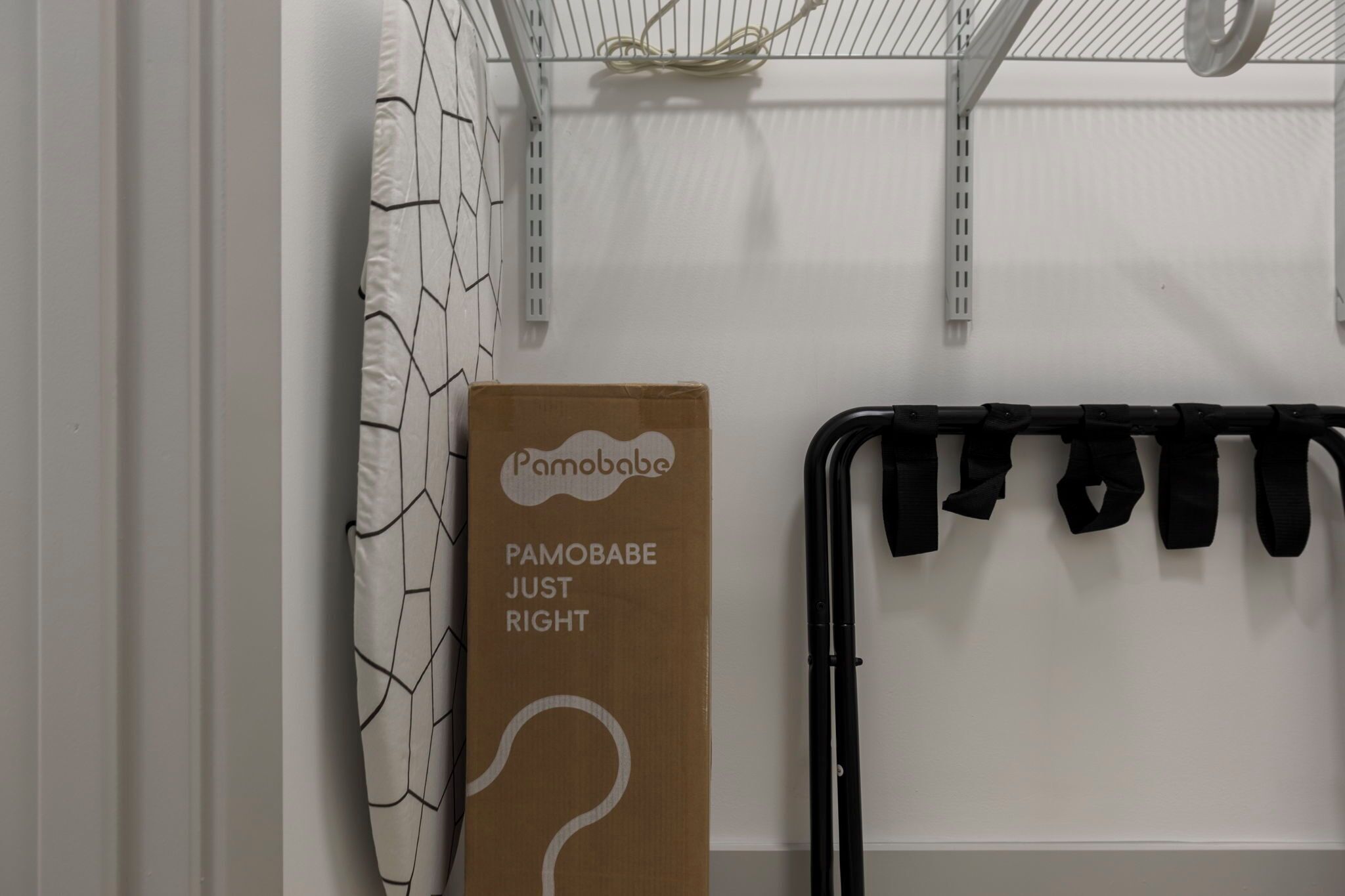 Et værelse med et hvidt gardin, en papkasse med påskriften 'Pamobabe Just Right', og et sort metalstativ med slips.