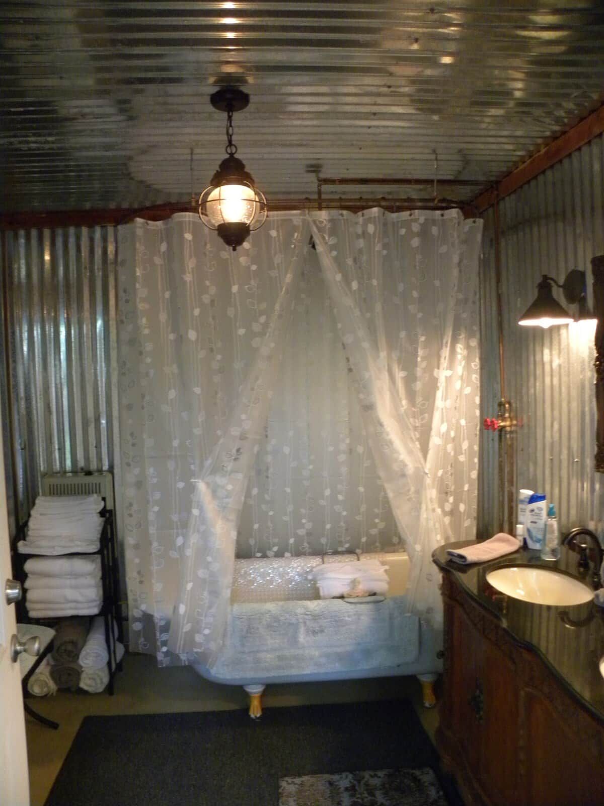 A bedroom with a canopy bed, a bedside table, a mirror, and a bathroom with a sink and toilet.