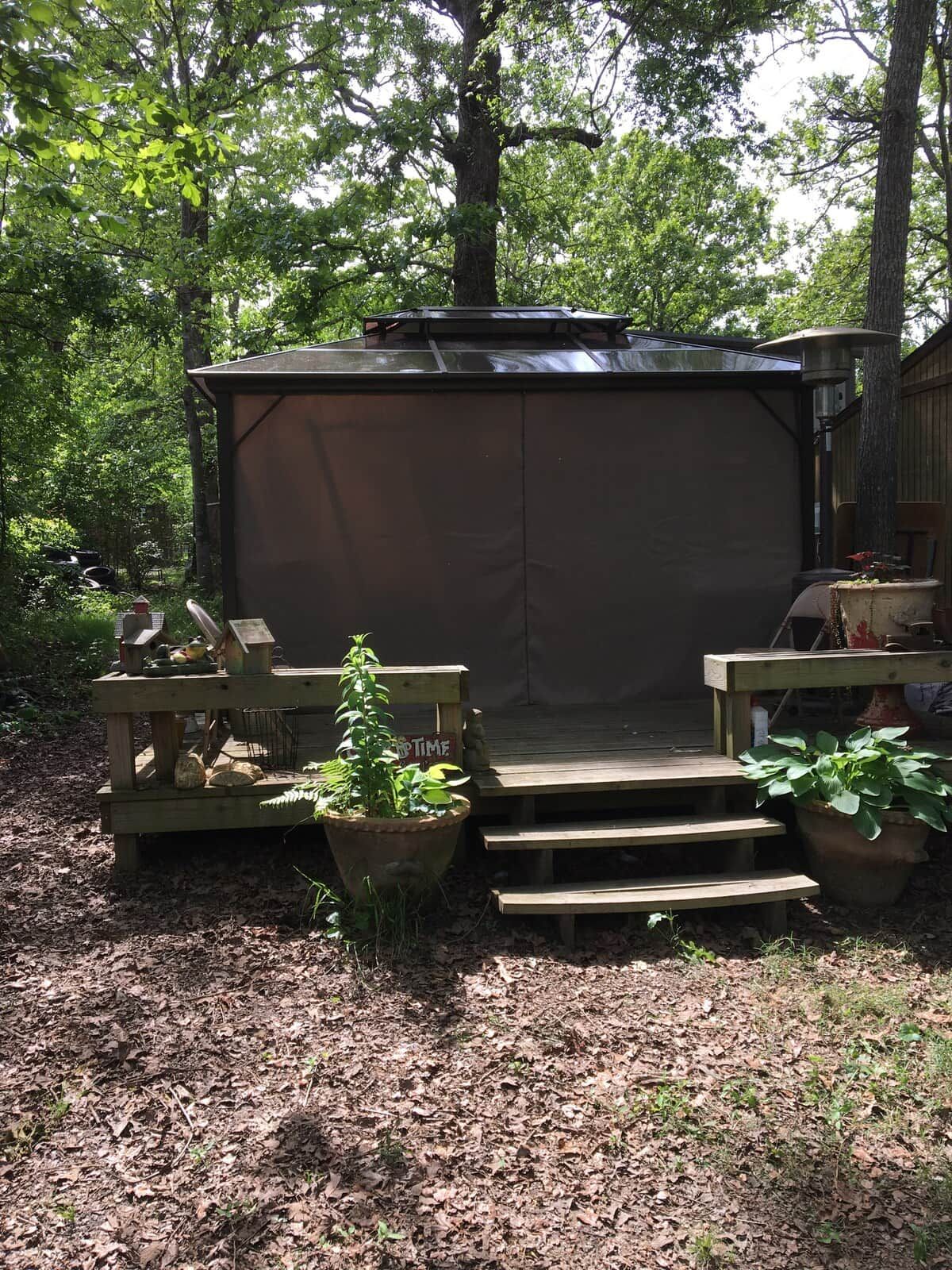 Un espace extérieur aménagé, abrité et doté d’un banc en bois et d’une table, entouré de plantes en pot et d’une terrasse en bois.