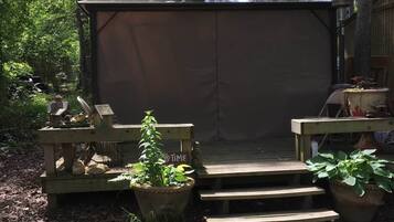 Un espace extérieur aménagé, abrité et doté d’un banc en bois et d’une table, entouré de plantes en pot et d’une terrasse en bois.