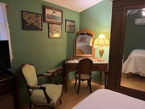 A room with a bed, a desk, a chair, a mirror, and framed pictures on the wall.