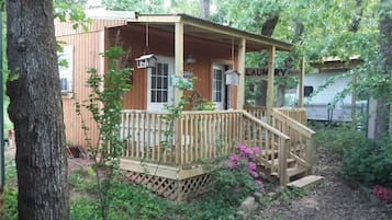 Une cabane en bois dotée d’un porche, entourée d’arbres et de végétation.