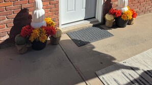 A brick building with a white door, a wreath, and decorative pumpkins and flowers on the ground.