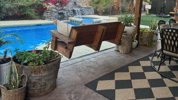 A covered patio with a pool, wooden seating, potted plants, and a stone wall with a waterfall feature. - Cozy 1-bedroom studio in gorgeous El Paso (El Paso)