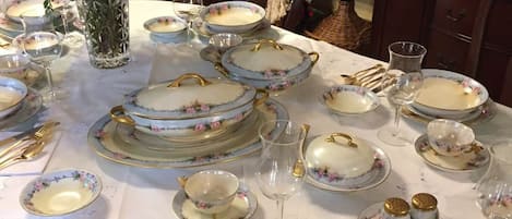 Une table à manger dressée avec des assiettes ornées de motifs floraux, des couverts dorés et un vase rempli de fleurs jaunes.