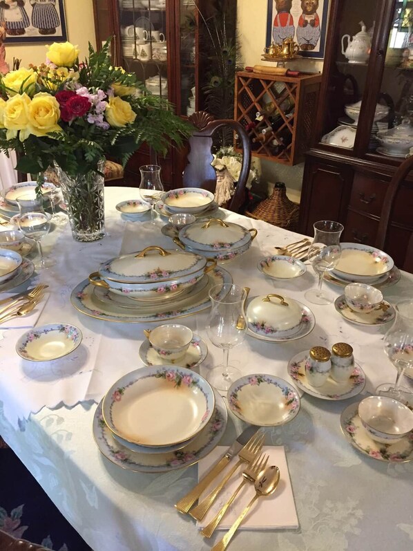 A dining table set with floral-patterned plates, gold cutlery, and a vase of yellow flowers.