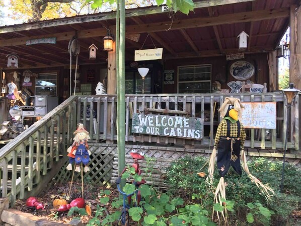 A rustic cabin with a wooden porch, a welcome sign, and a birdhouse.