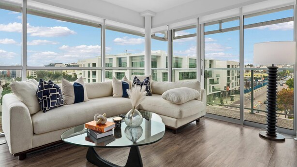 A modern living room with a glass coffee table, a beige sofa, and a view of a cityscape through large windows. - Anse Lasio' Penthouse Panoramic Ocean View Rooftop BBQ, Pool and Gym (Santa Monica)