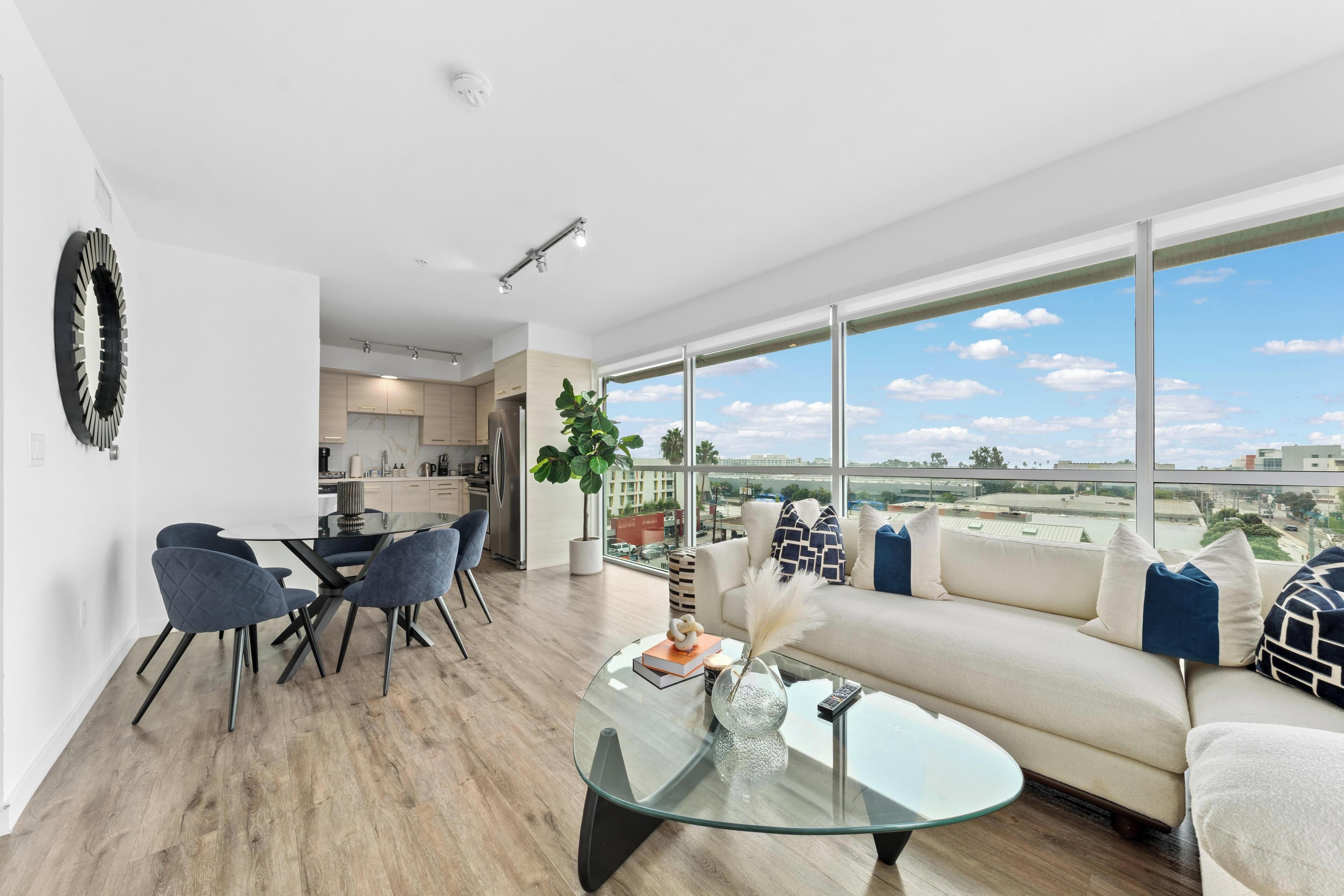 A modern living room with a glass coffee table, a sofa, and a dining area with chairs.