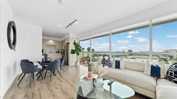 A modern living room with a glass coffee table, a sofa, and a dining area with chairs.