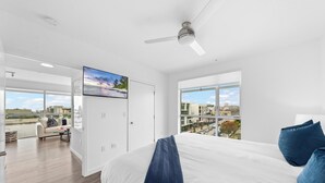A modern hotel room with a large bed, a ceiling fan, and a city view through large windows. - Anse Lasio' Penthouse Panoramic Ocean View Rooftop BBQ, Pool and Gym (Santa Monica)