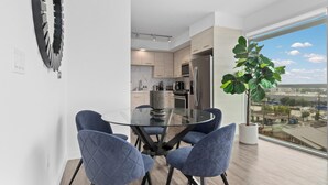 A modern kitchen with a dining area, a large window with a city view, and a potted plant. - Anse Lasio' Penthouse Panoramic Ocean View Rooftop BBQ, Pool and Gym (Santa Monica)