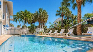 A swimming pool with clear water, surrounded by palm trees and lounge chairs. - Turtle Tide at Del Mar - Charming Condo w/ Heated Pool, Beach Equipment, & Steps To The Beach (Indian Rocks Beach)
