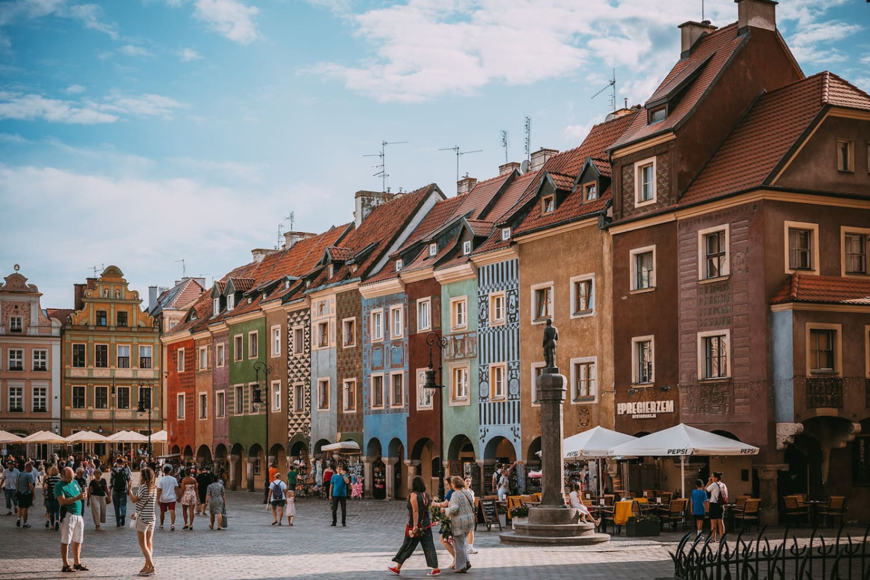 Una plaza histórica con edificios coloridos, mesas al aire libre y una fuente central.