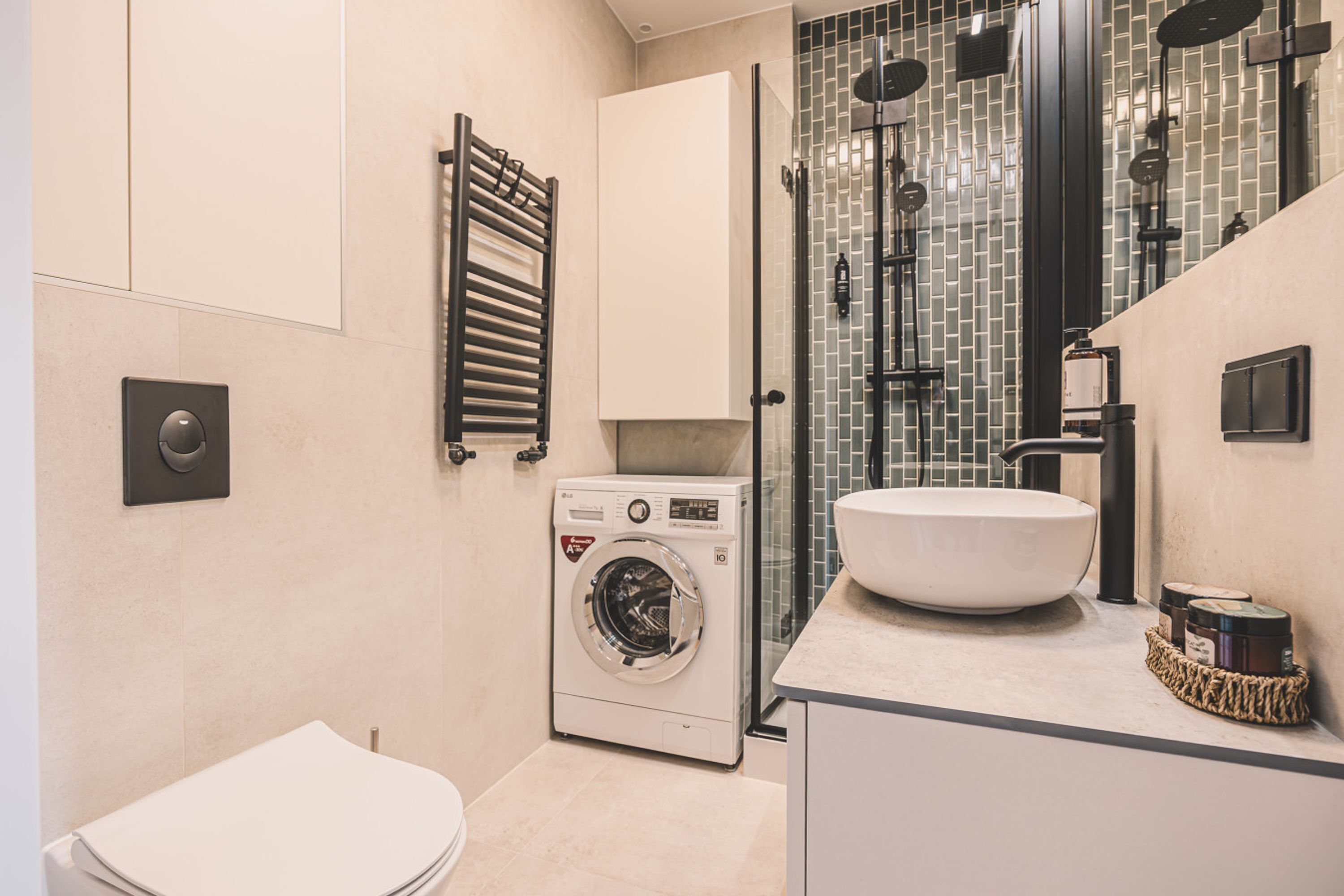 A modern bathroom with a built-in washing machine, a large sink, and a glass shower enclosure.