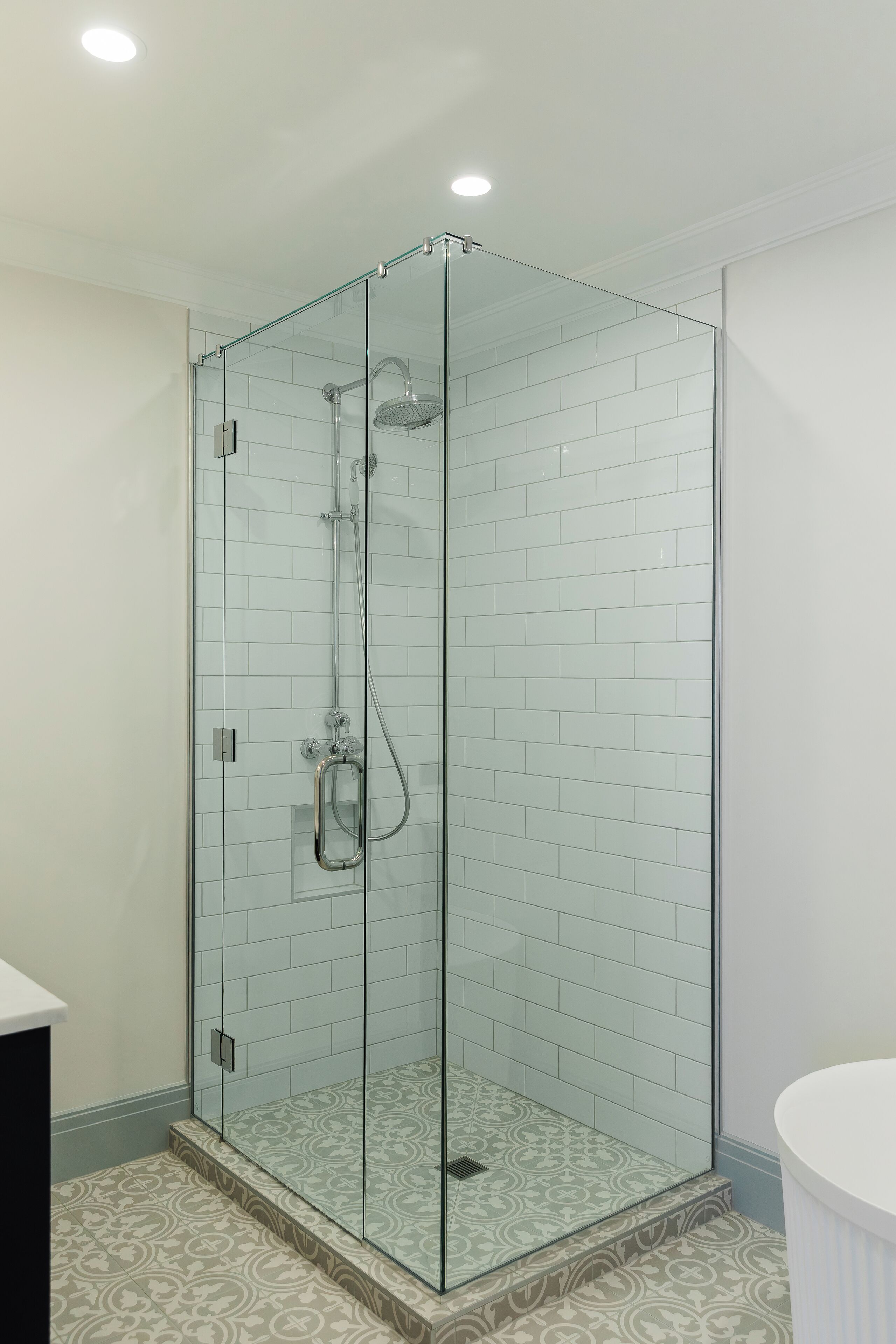 Ducha con cerramiento de vidrio, suelo de azulejos y un lavamanos blanco a la derecha.