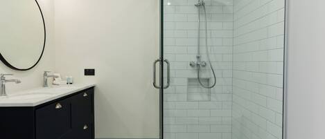 A modern bathroom with a glass-enclosed shower, a black vanity with a mirror, and patterned floor tiles.